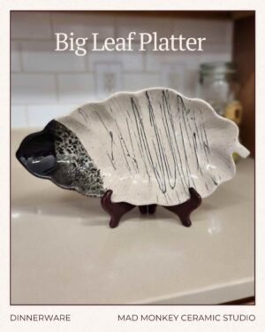 Handmade black and white ceramic big leaf serving platter by Mad Monkey Ceramic Studio in Red Deer, featuring bold black glaze drips and speckles on a white speckled body, shown on a wooden stand